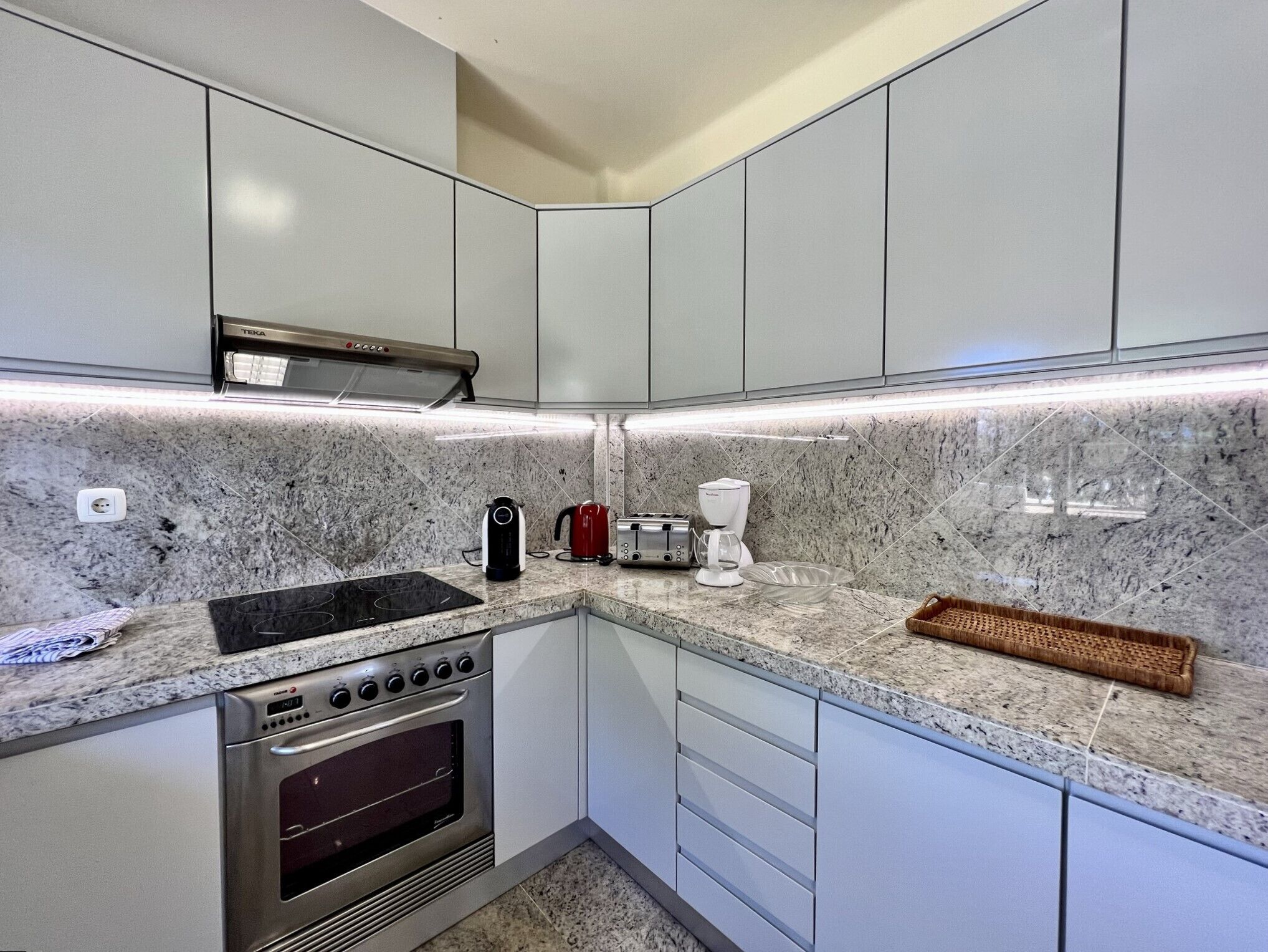A modern kitchen with white cabinets, a built-in oven, a stovetop, and a coffee maker.