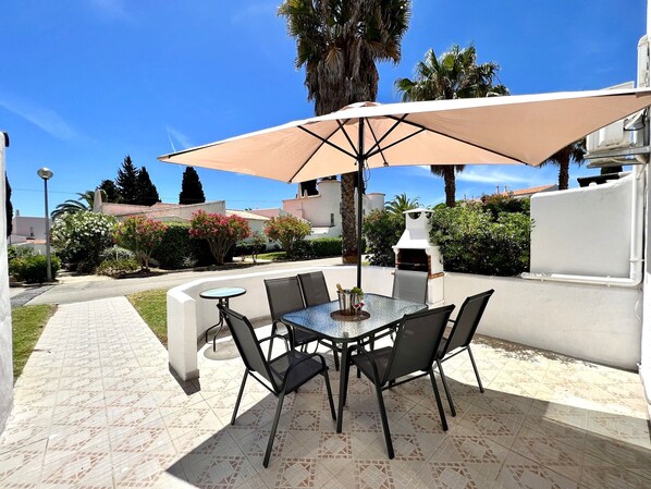 An outdoor patio with a round table and chairs, a large umbrella, and a barbecue grill. - Armação DE Pêra Twins 3 With Pool (Lagoa)