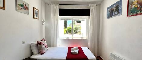Habitación de hotel con dos camas, una ventana con cortinas, un radiador y cuadros en las paredes.