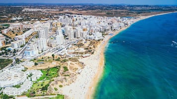 Vista aérea de una ciudad costera con imponentes edificios altos, una playa arenosa y un mar azul cristalino.