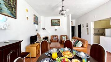 A dining area with a table set for breakfast, including plates, cutlery, and a variety of fruits and pastries.