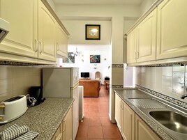Una cocina con armarios de tonos claros, encimera de granito y salpicadero de azulejos. Se observan un refrigerador, un lavamanos y un tostador en la encimera.