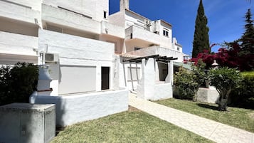 Un edificio blanco con varios balcones, un espacio exterior cubierto y un césped bien cuidado.