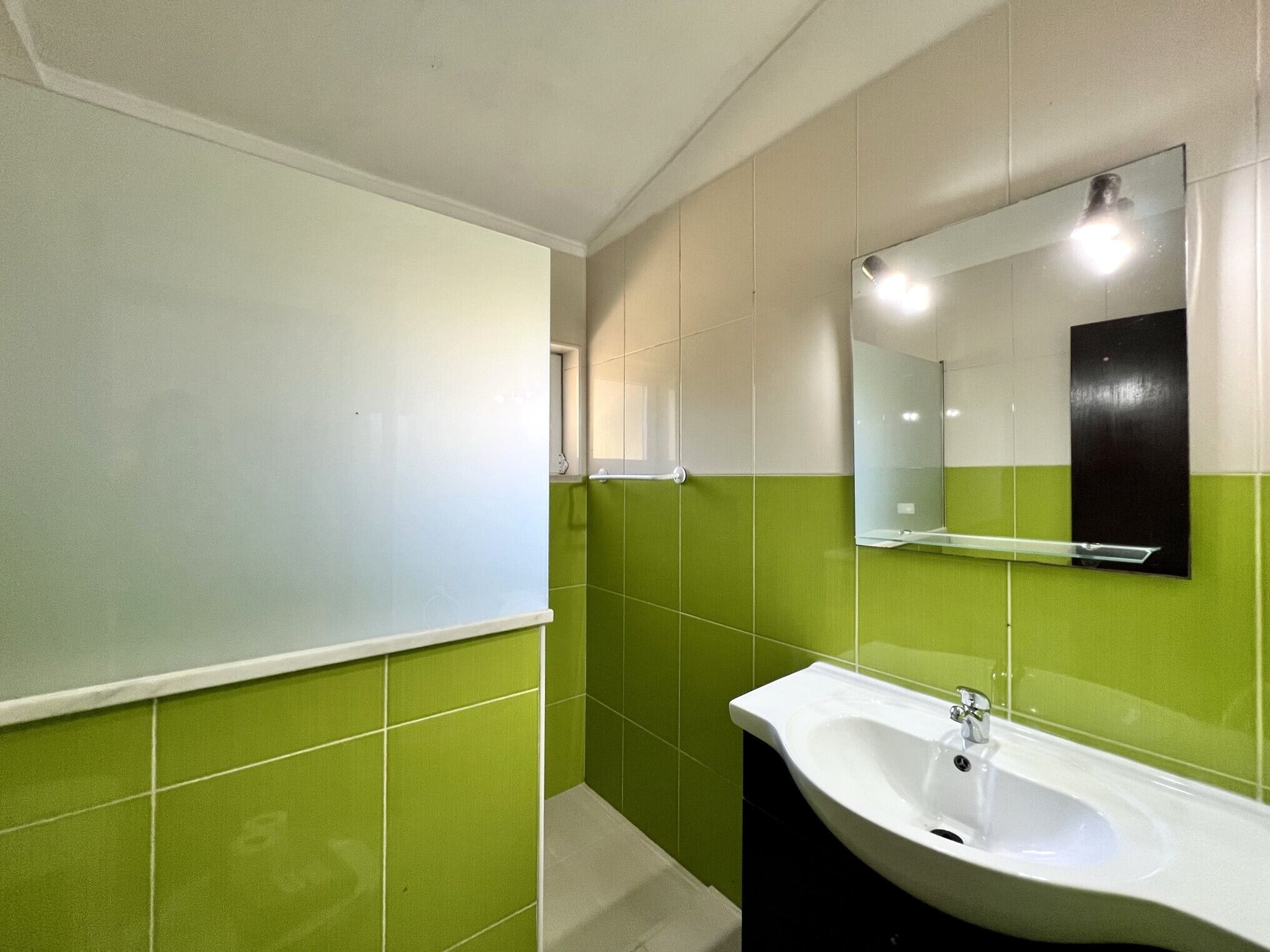 A bathroom with green and white tiles, a white sink, and a mirror.