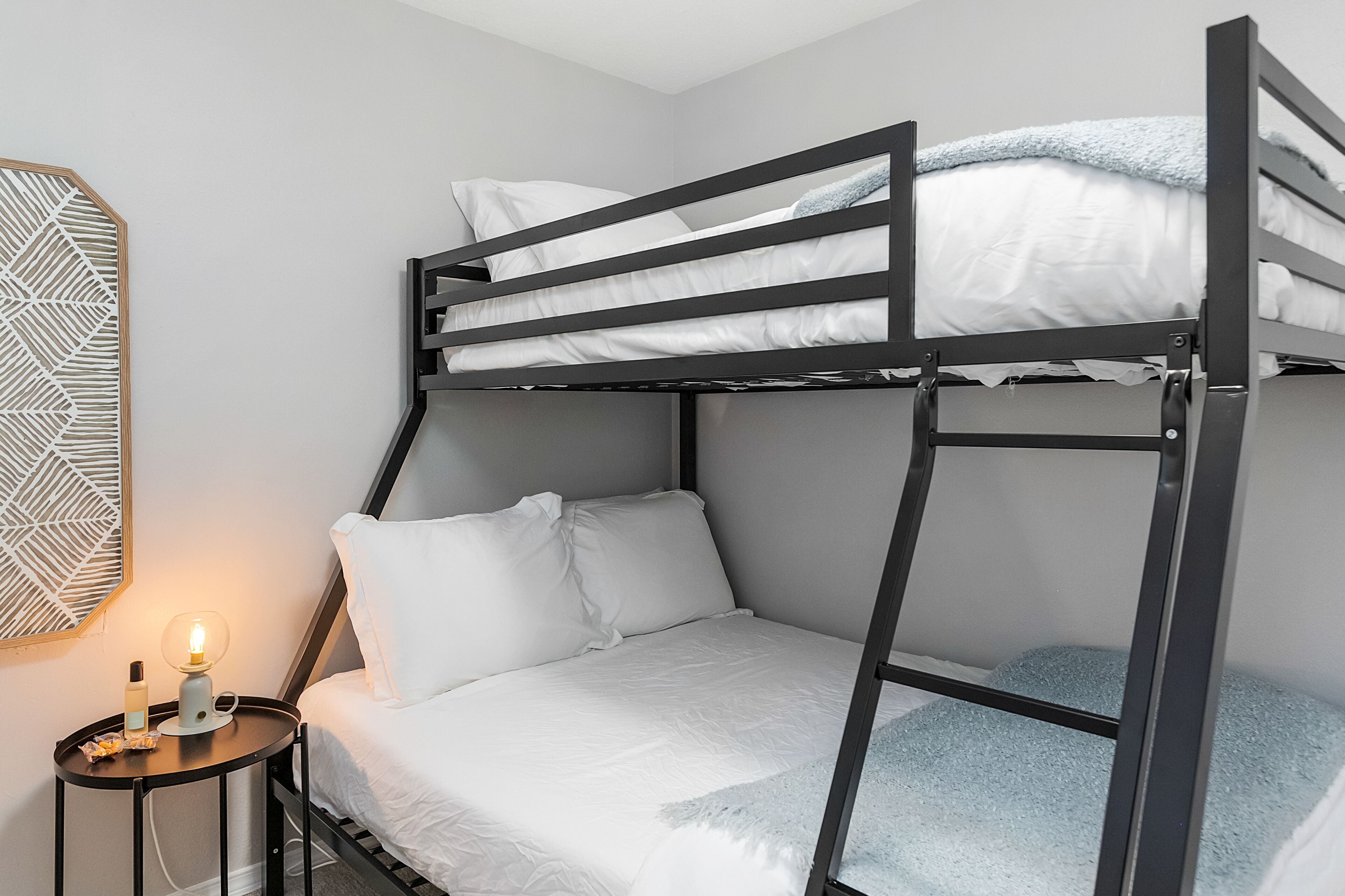 A bunk bed with white bedding and a small bedside table with a lamp.
