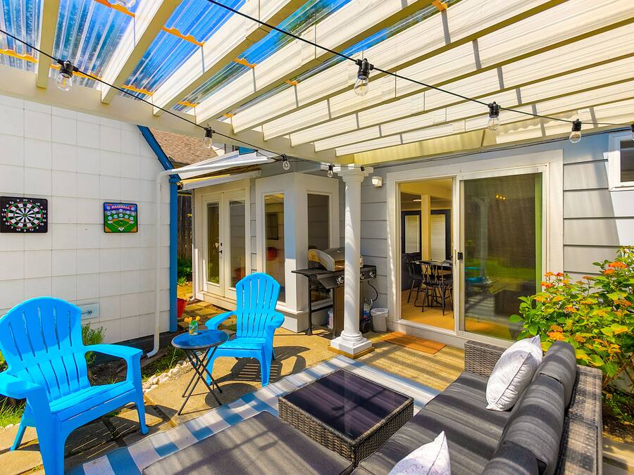 A covered patio with blue chairs, a sofa, and a dining table.
