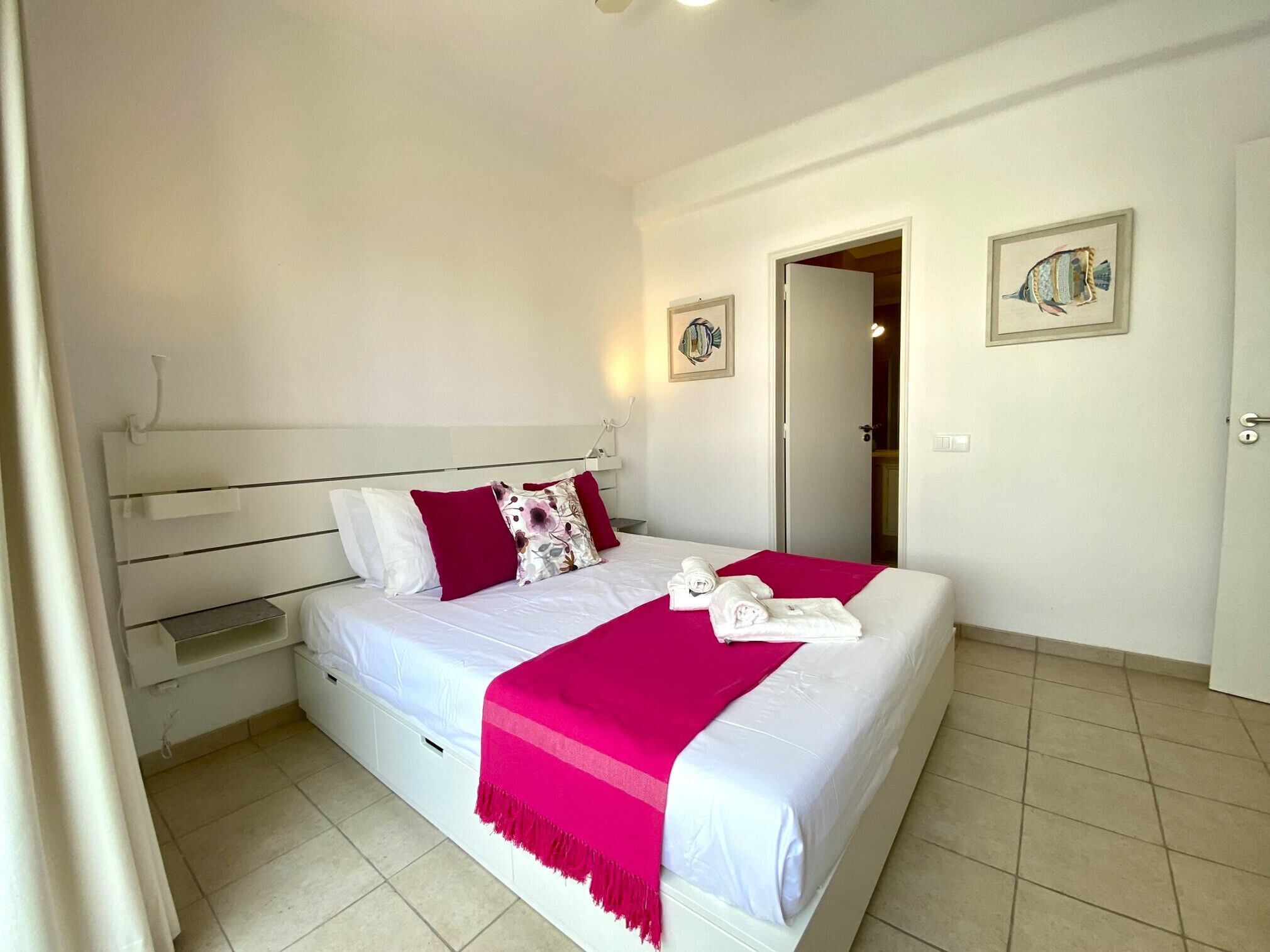 Une chambre à coucher bien rangée, avec un lit, des oreillers, une table de chevet et une porte donnant sur une autre pièce.