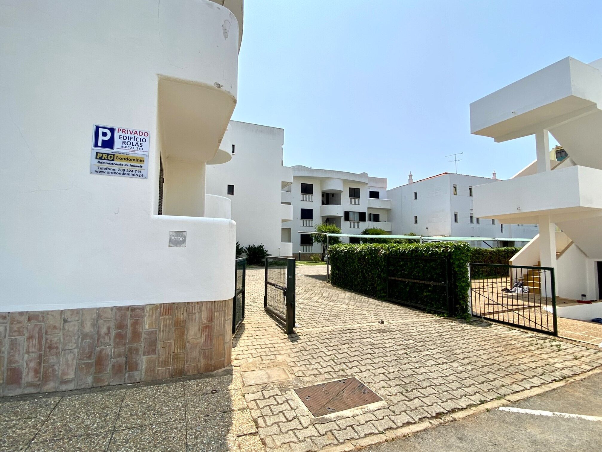 Un immeuble résidentiel avec un panneau indiquant un espace de stationnement privé, un chemin piétonnier pavé et une entrée fermée par un portail.