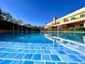 A swimming pool with blue tiles, surrounded by a building with balconies and a clear blue sky. - Vilamoura Paradise Golf With Pool (Loulé)