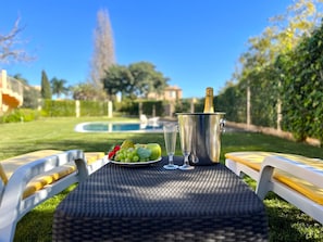 An outdoor dining setup with a metal table, two chairs, a bottle of champagne, and a plate of fruit. - Vilamoura Paradise Golf With Pool (Loulé)