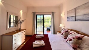 Hotellihuone, jossa on sänky, lipasto, peili, ikkuna verhoilla, tuoli ja taulu seinällä.