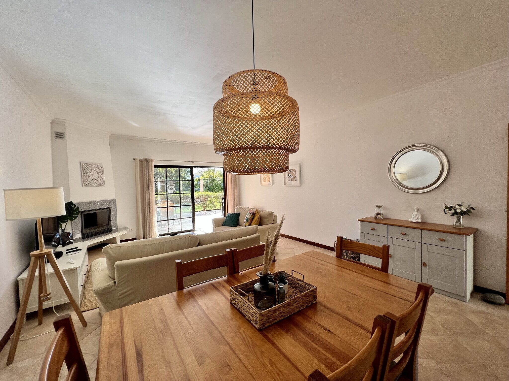 Una sala de estar moderna con una mesa de comedor de madera, sofá y un ventanal con vistas a la vegetación.