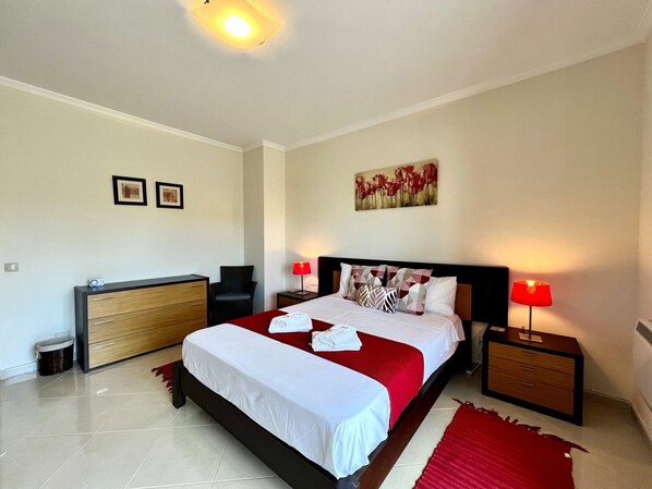 A hotel room with a bed, a dresser, a chair, and a nightstand with a lamp. - Pêra Brightness Villa by Homing (Silves)