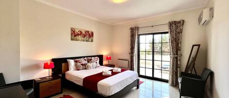 A bedroom with a bed, nightstands, a red rug, a painting, a window with curtains, and a chair.