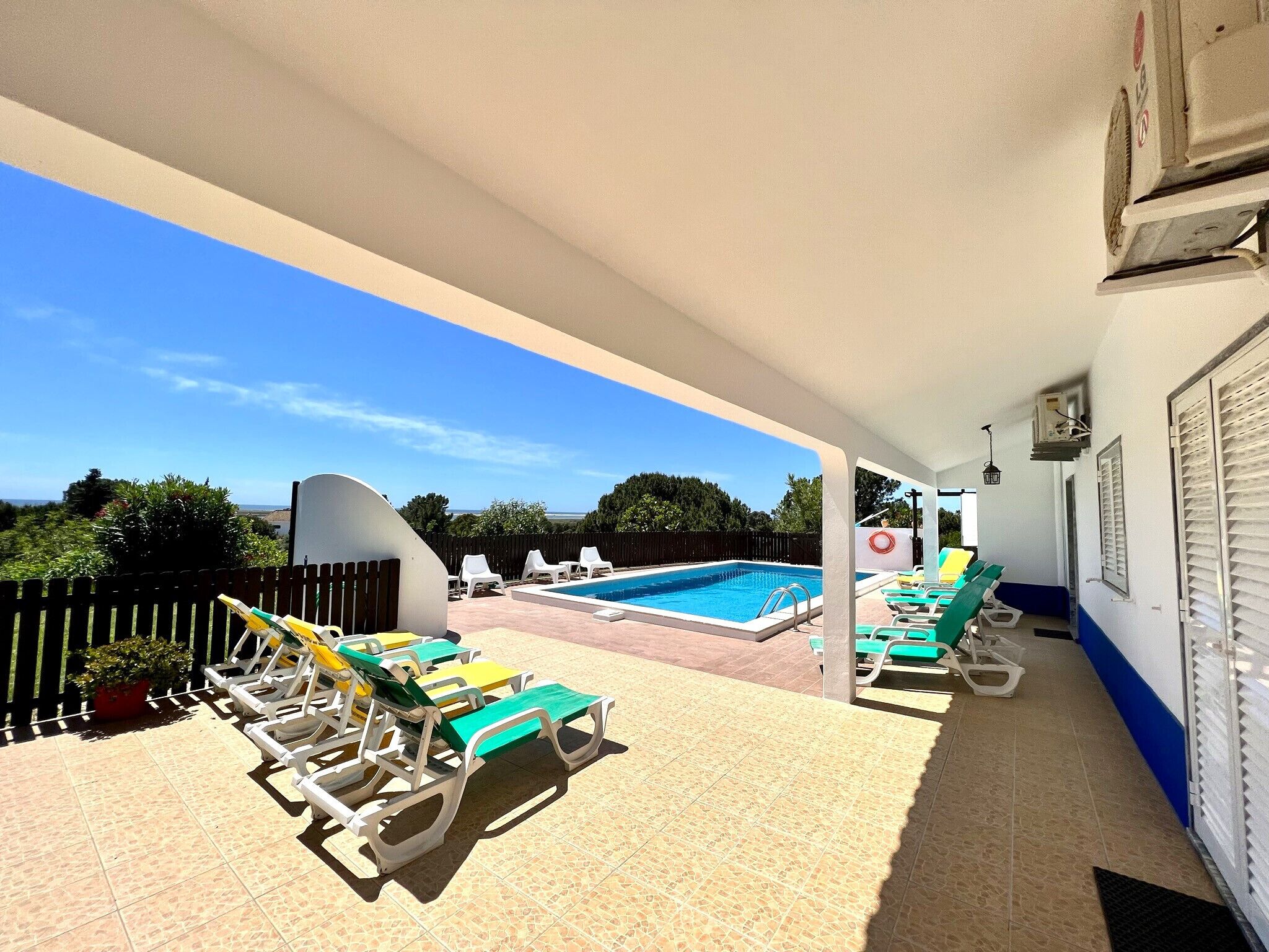 A covered outdoor area with a pool, lounge chairs, and a view of the sea.