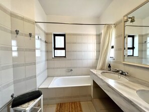 A modern bathroom with a bathtub, a large mirror, and a window.