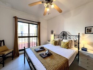 A bedroom with a bed, a nightstand, a chair, a window with curtains, and a ceiling fan.
