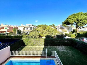 A swimming pool with a white fence, surrounded by well-maintained grass and trees.