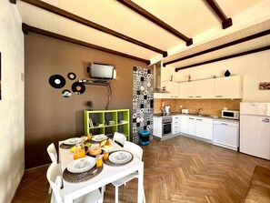 Eine kompakte Küche mit weißen Schränken, einer Mikrowelle und einem Geschirrspüler. Ein Esstisch ist mit Tellern und Gläsern gedeckt, und an der Wand ist ein Fernseher angebracht.