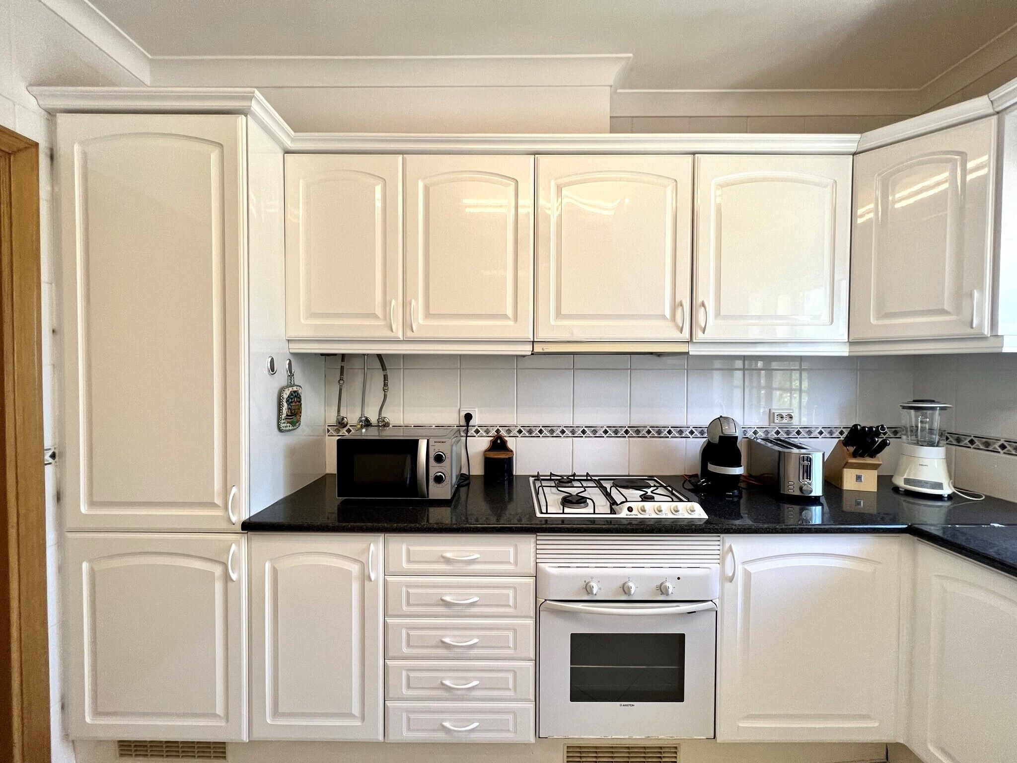 A kitchen with white cabinets, a gas stove, a microwave, a toaster, and a blender.