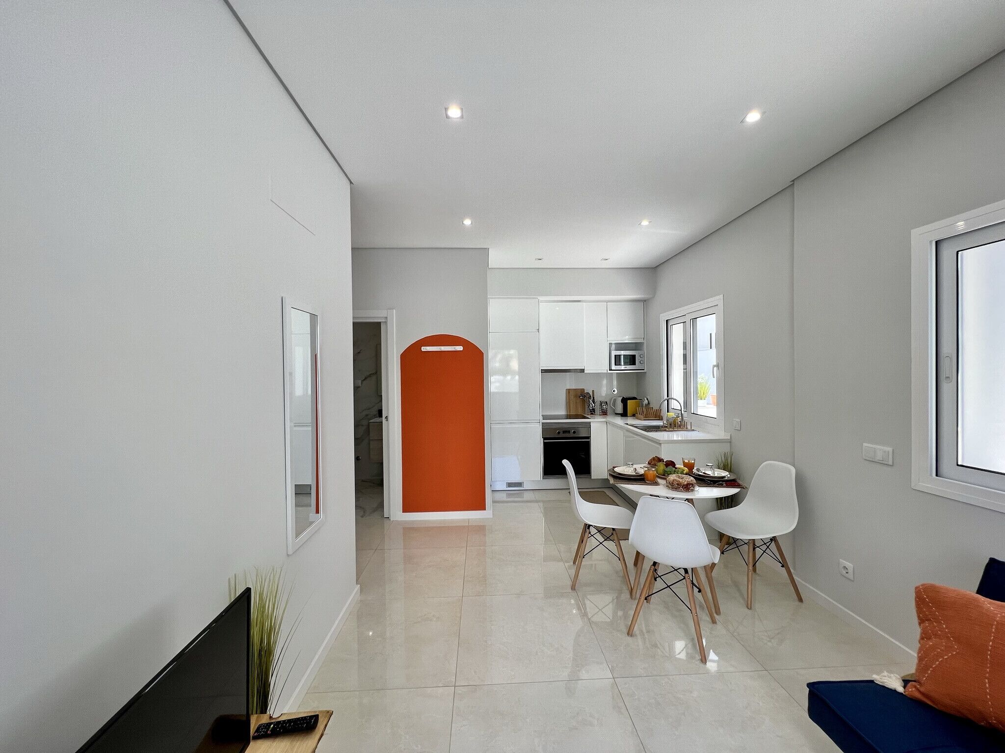 A modern kitchen with white cabinets, a microwave, and a dining area with white chairs and a table.
