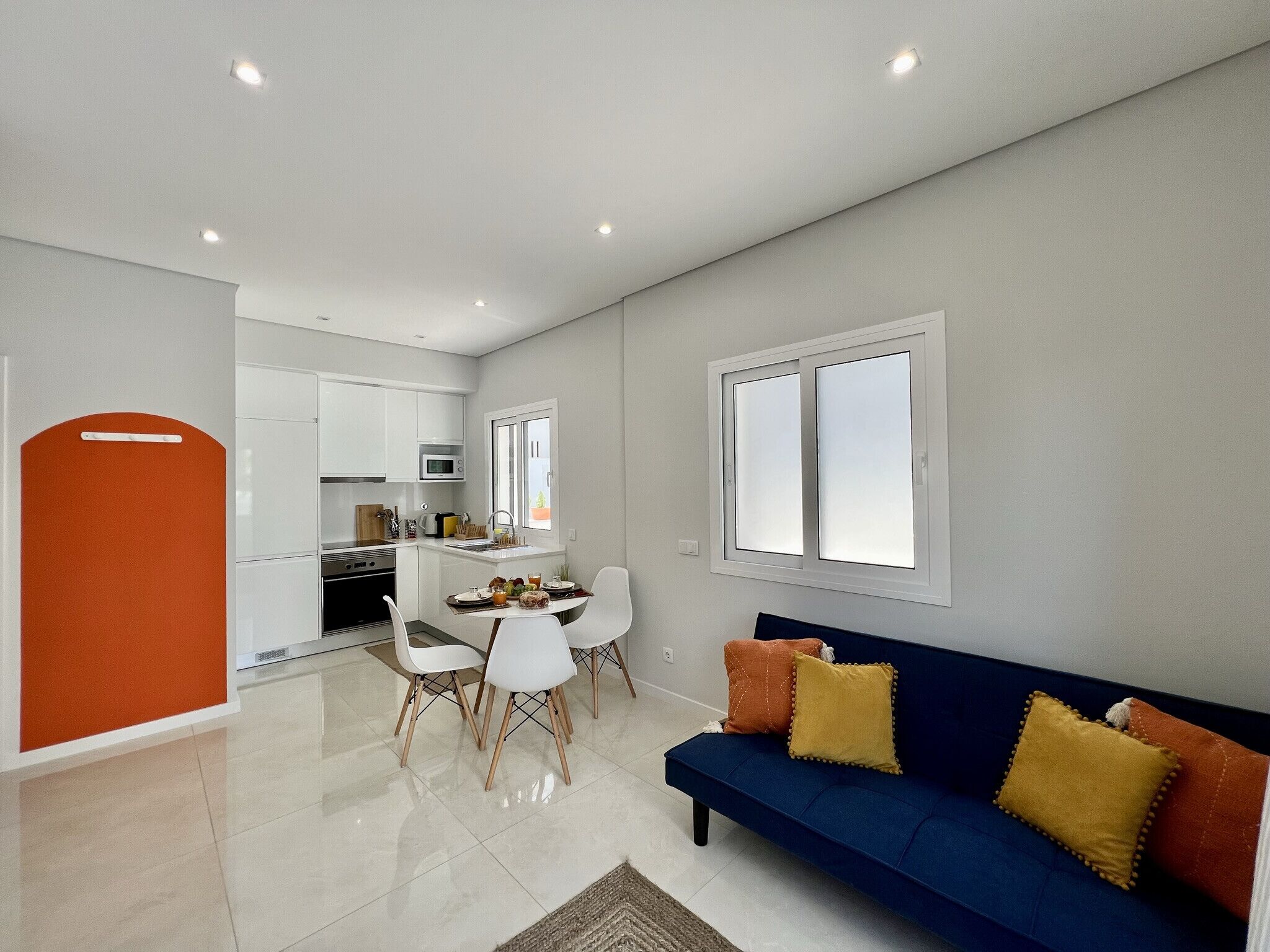 Una cocina moderna con armarios blancos, un área de comedor con mesa y sillas, y un sofá azul con cojines.