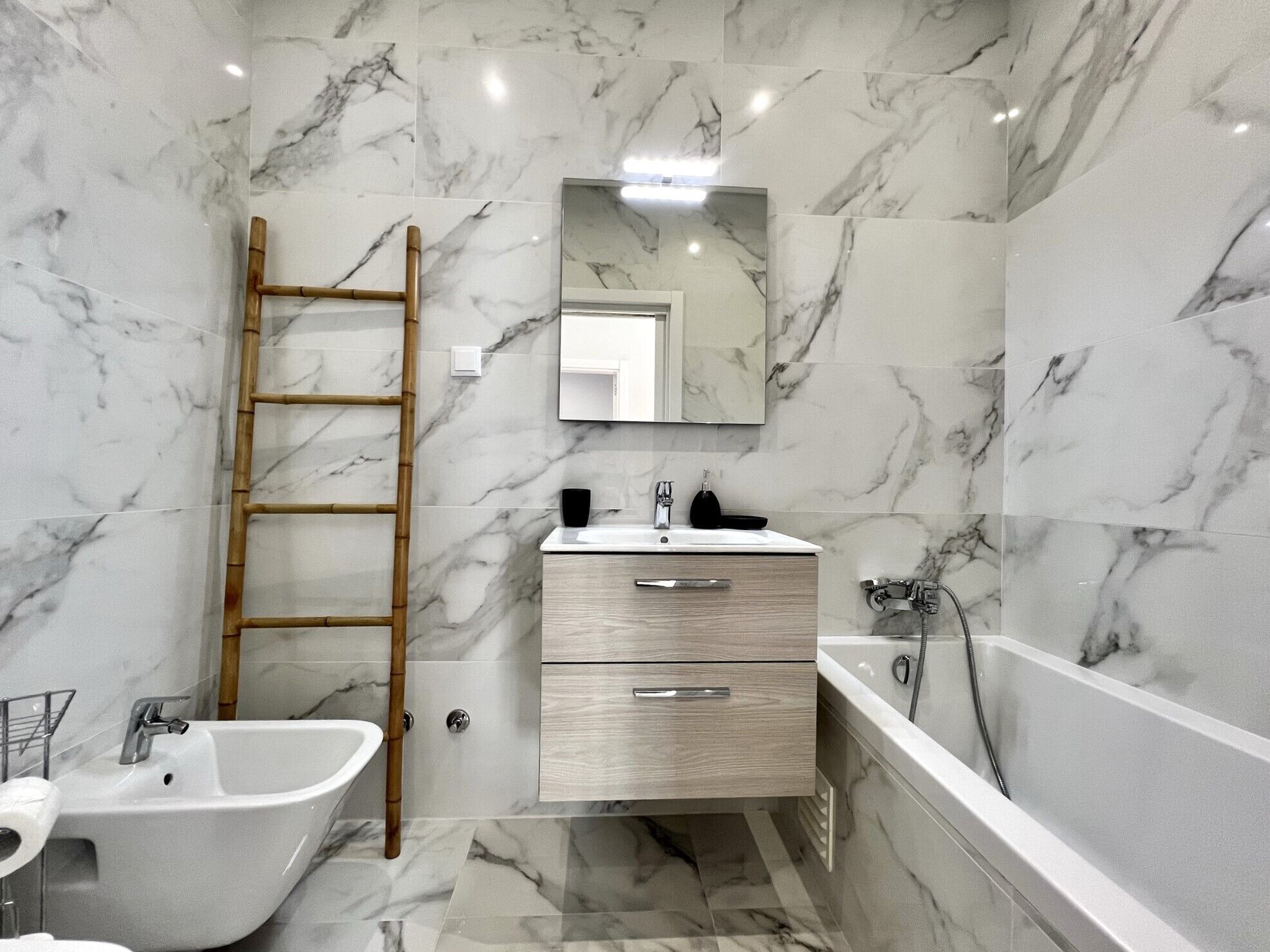 A bathroom with marble walls, a wooden ladder, a sink, a mirror, and a bathtub.