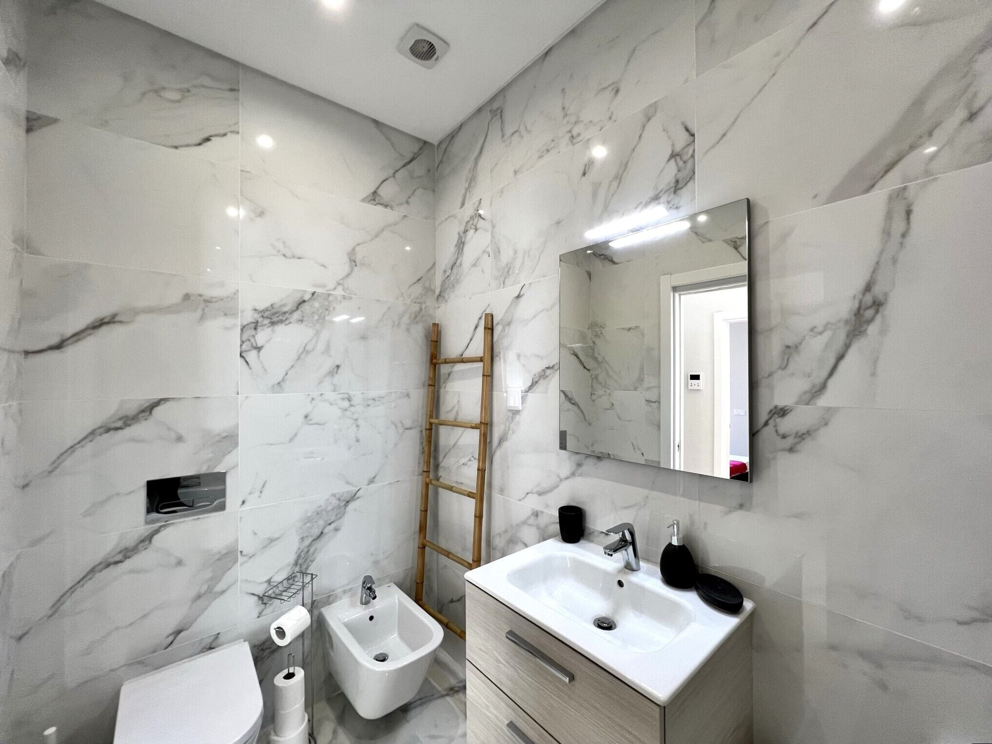 Et moderne badeværelse med marmorvægge, en bidet, en vask og et spejl.
