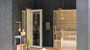 A modern building entrance with a glass door, a wooden bench, and a small table with a plant. - Lovely home in Ebeltoft with sauna (Ebeltoft)