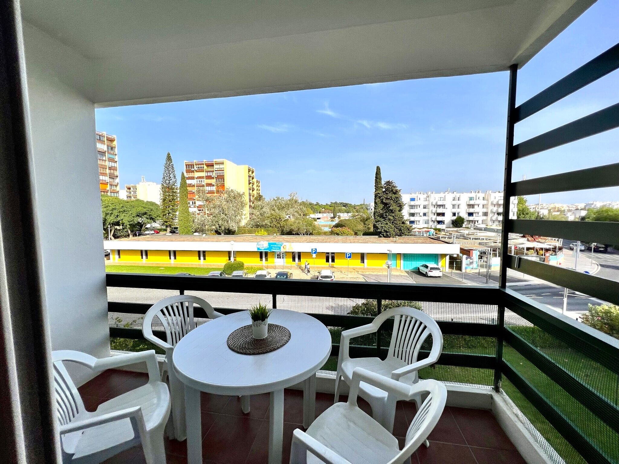 A balcony with a table and chairs, overlooking a parking area and buildings.