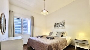 A bedroom with a bed, a bedside table, a lamp, a window with curtains, and a wall-mounted artwork. - Vilamoura Central 4 With Pool by Homing (Loulé)