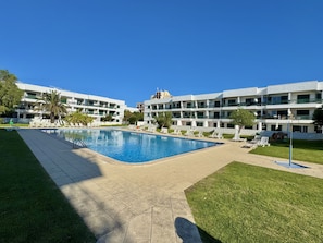 Ein Hotel mit Schwimmbad, umgeben von Liegestühlen und Palmen.