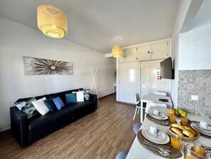 Ein modernes Wohnzimmer mit einer schwarzen Couch, einem Esstisch gedeckt mit Tellern, Gläsern und einer Obstschale.