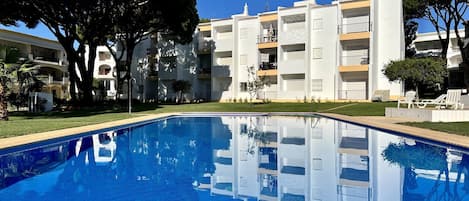 Piscina com superfície de água azul cristalina, rodeada por um gramado bem cuidado e árvores.
