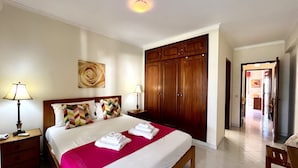 A hotel bedroom with a large bed, wooden wardrobe, and a view of the hallway. - Vilamoura Garden View 1 With Pool (Loulé)