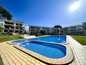 Ein Schwimmbecken mit Fliesen umgeben von einem Gebäude mit mehreren Balkonen und blauem Himmel.