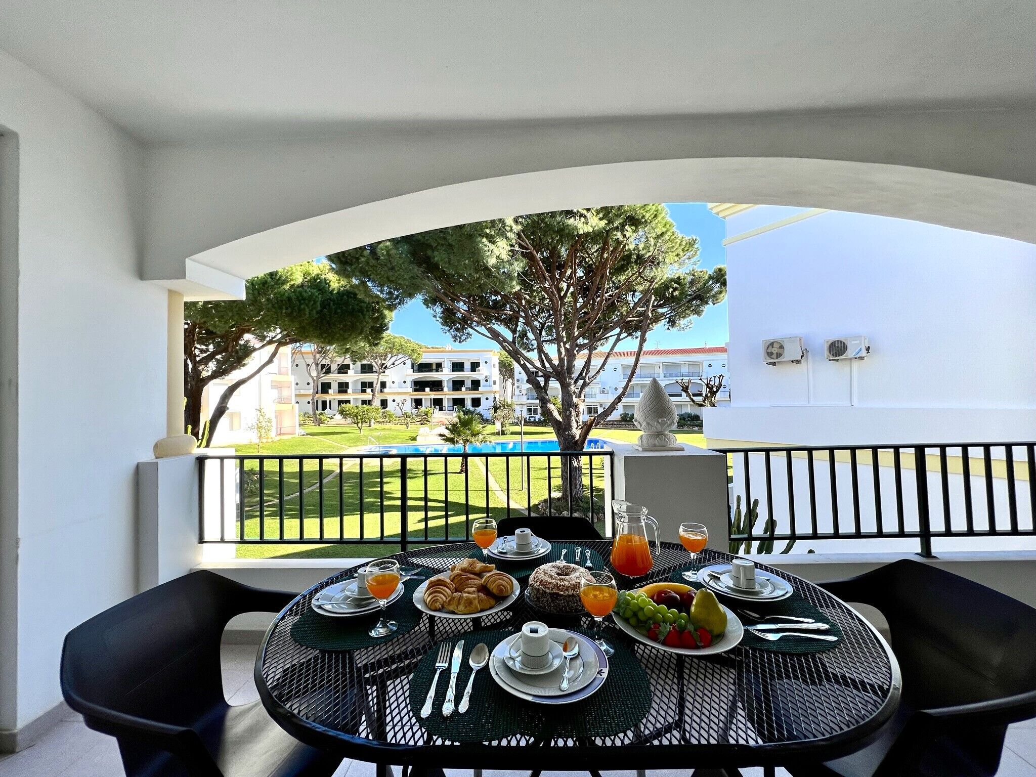 Un balcone con un tavolo apparecchiato per la colazione, vista su una piscina e un edificio.