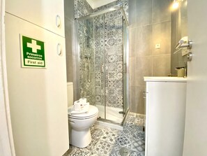 A bathroom with a shower, toilet, and a first aid sign.