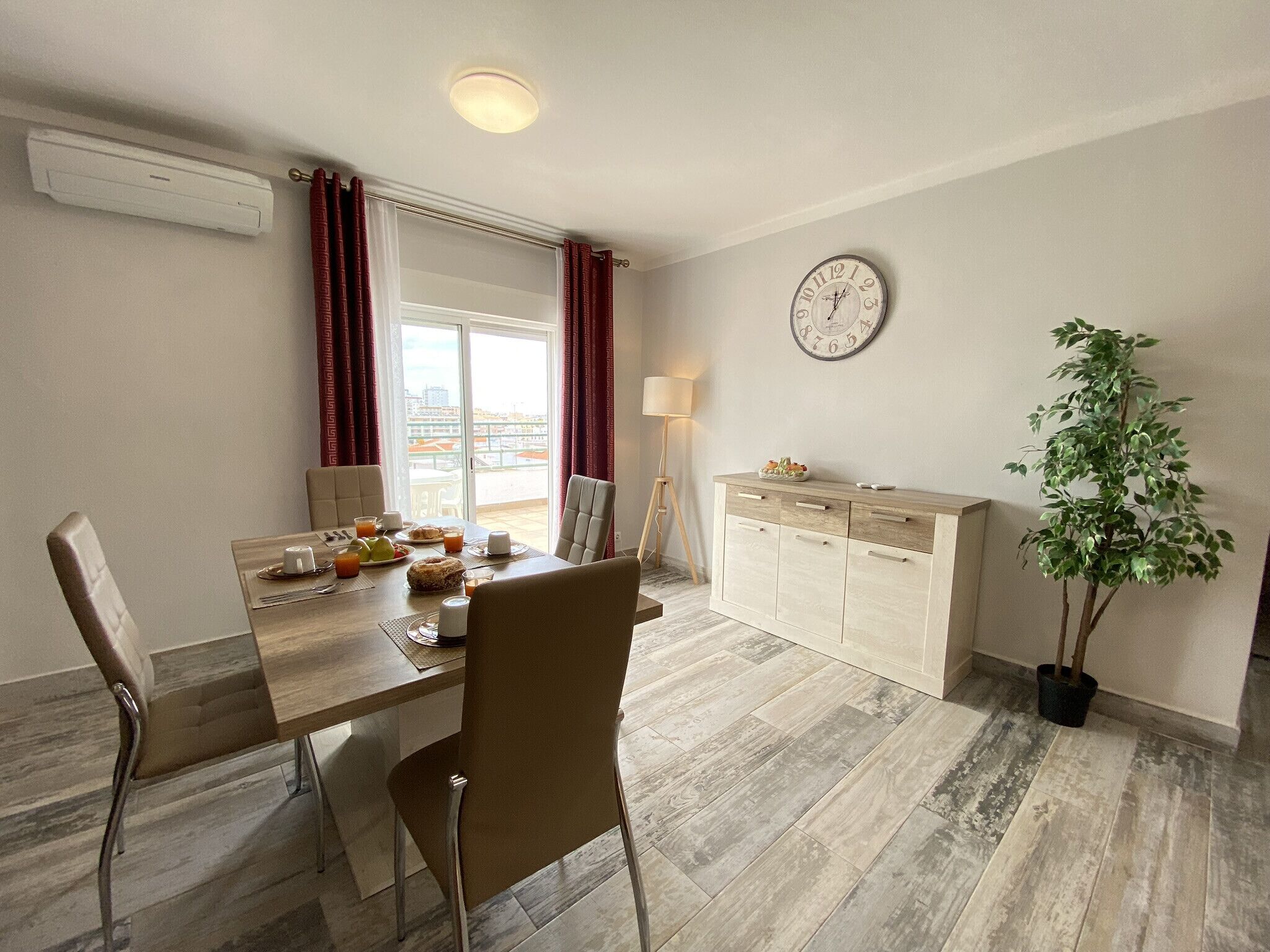 Un coin repas avec une table dressée pour deux personnes, une horloge au mur et une plante en pot.