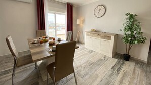 A dining area with a table set for two, a clock on the wall, and a potted plant. - Quarteira Ocean Breeze 2 by Homing (Loulé)