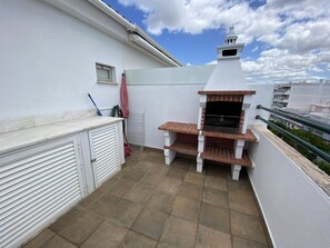 A rooftop terrace with a barbecue grill, a small window, and a white railing. - Quarteira Ocean Breeze 2 by Homing (Loulé)
