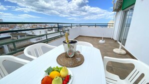 A balcony with a table set for a meal, a bottle of champagne, and a plate of fruit. - Quarteira Ocean Breeze 2 by Homing (Loulé)