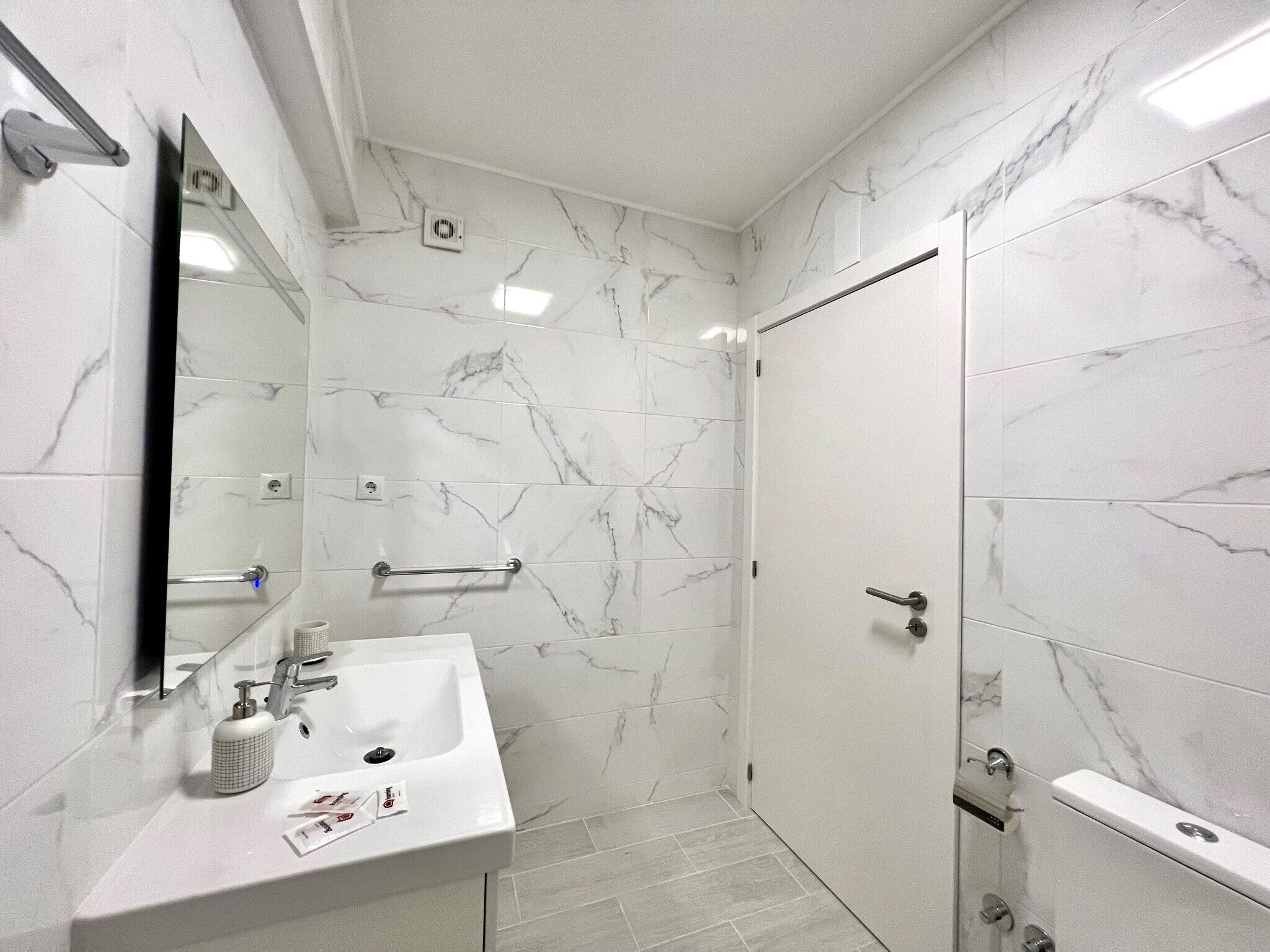 A modern bathroom with a marble floor, a sink with a mirror, a towel rack, and a shower area.
