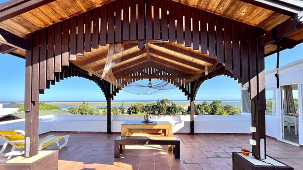 A covered outdoor area with a wooden pergola, a table, and chairs. - Tavira Vila Formosa 6 With Pool (Tavira)