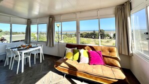 A sunlit room with a large window, a sofa, and a dining table. - Tavira Vila Formosa 6 With Pool (Tavira)