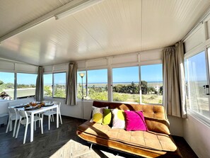 A sunlit room with a large window, a sofa, and a dining table. - Tavira Vila Formosa 6 With Pool (Tavira)