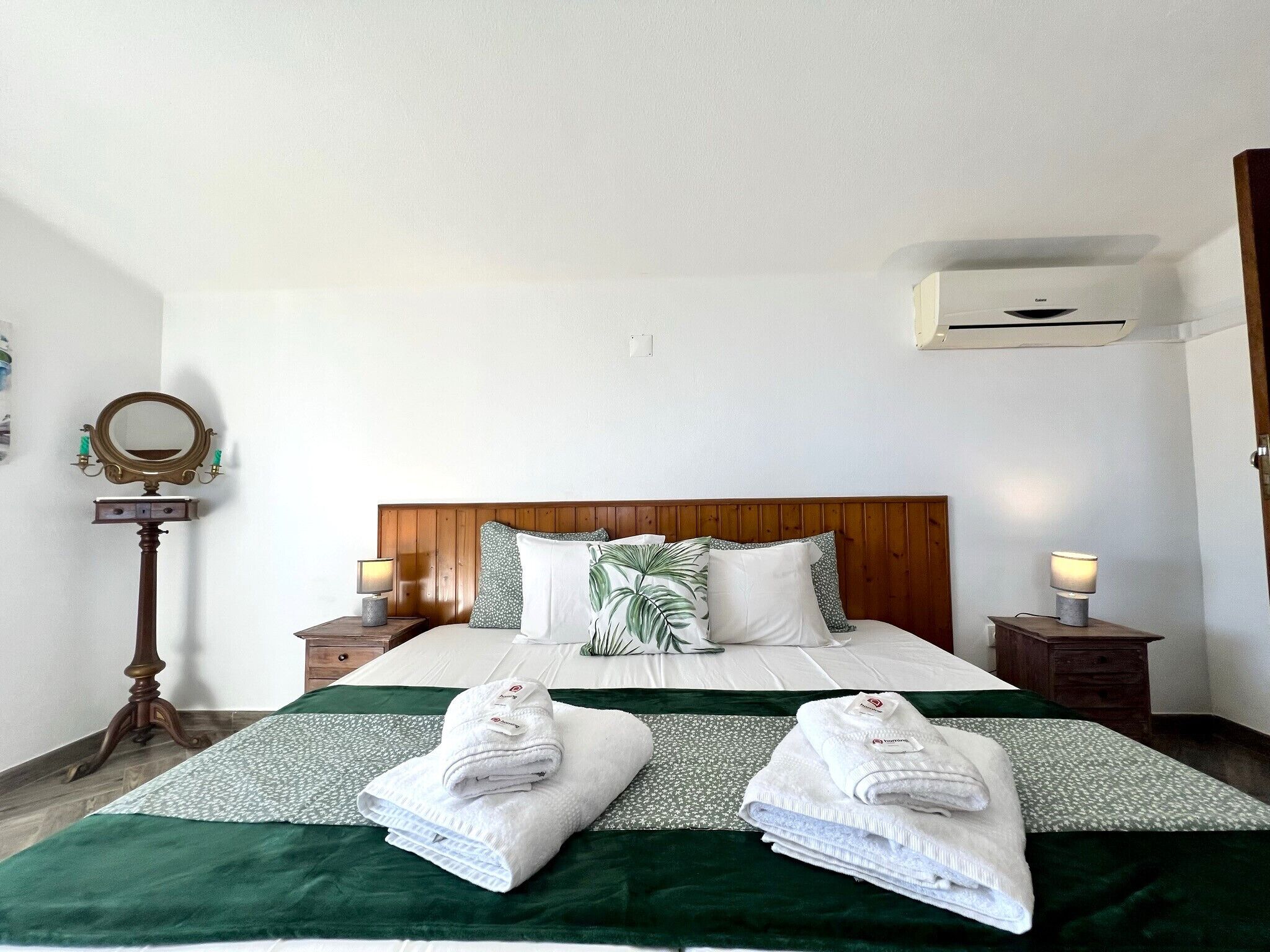 A hotel room with a wooden headboard, two bedside tables with lamps, a mirror, and two towels on the bed.