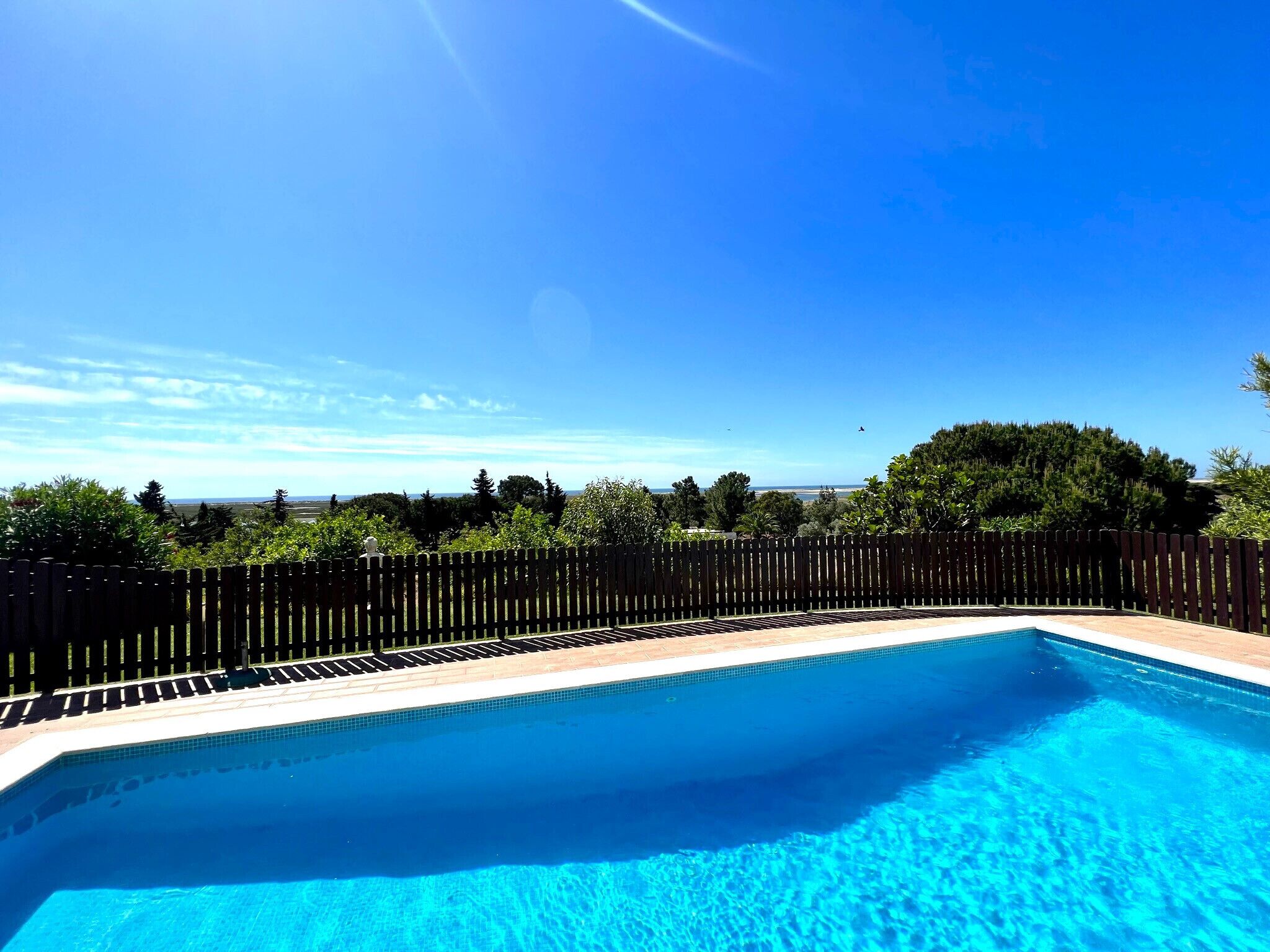 Une piscine d’un bleu éclatant, entourée d’une clôture en bois, et offrant une vue sur les arbres et un paysage lointain.