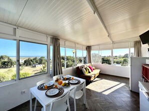 A sunlit room with a dining table set for breakfast, a sofa with cushions, and large windows offering a view of the outdoors. - Tavira Vila Formosa 6 With Pool (Tavira)