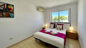 Un dormitorio con cama, dos mesitas de noche, una ventana con vistas y aire acondicionado, además de una obra de arte colgada en la pared.